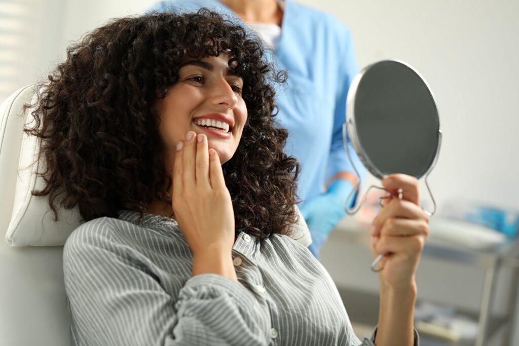 Woman with curly hair smiling at reflection in dental chair